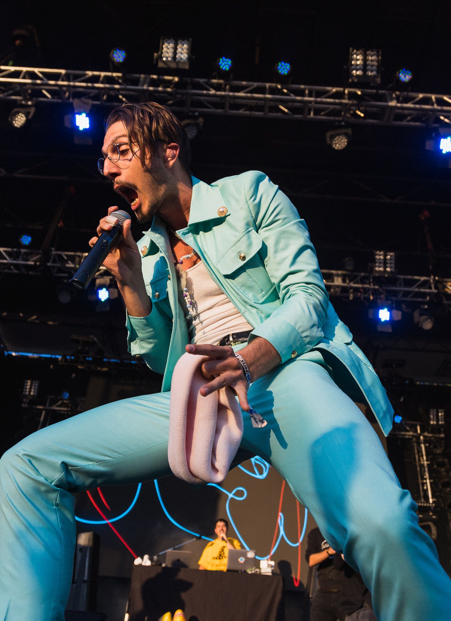Energetic performer in light blue suit singing on concert stage with dramatic lighting.