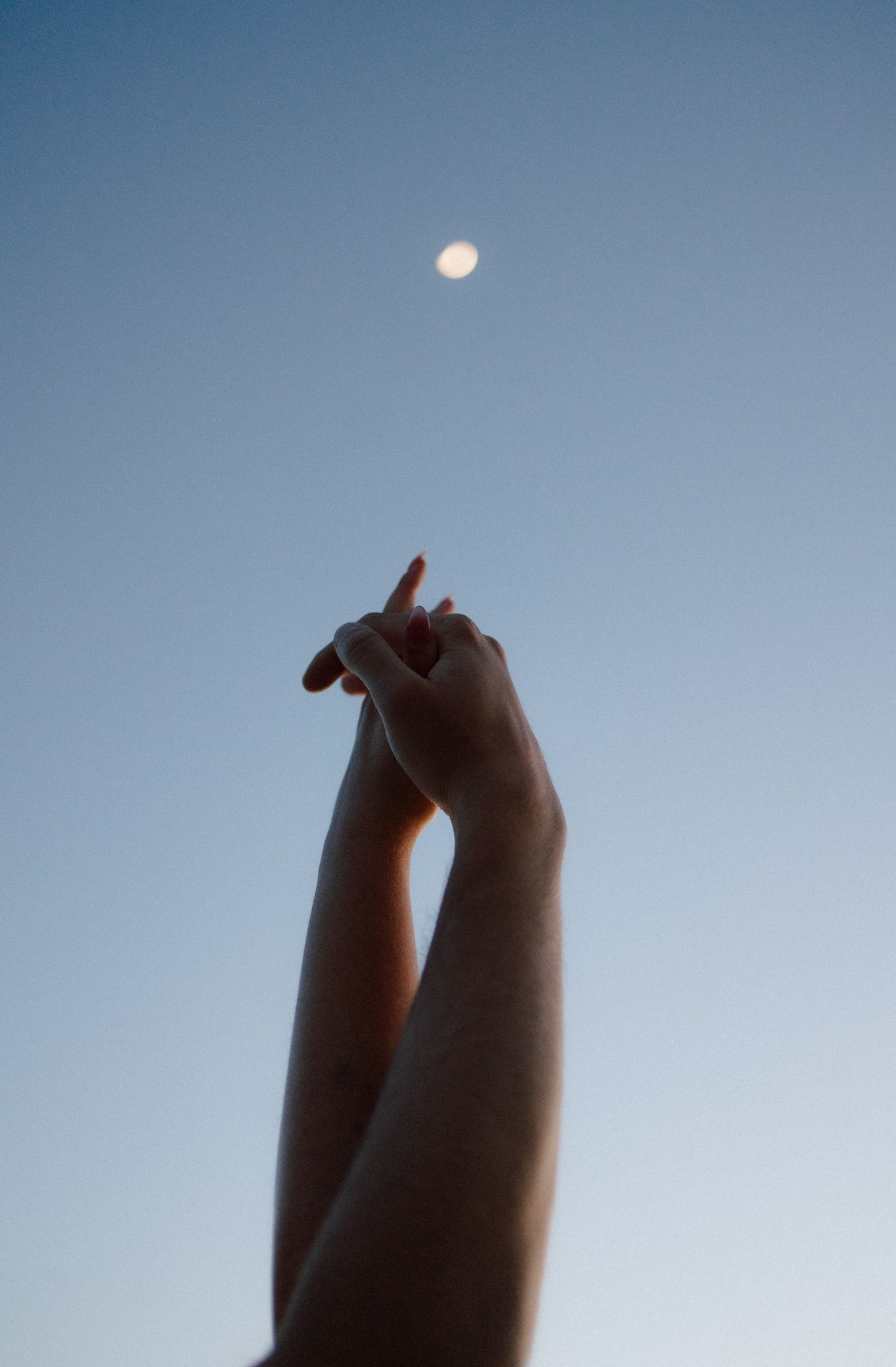 A sequence of silhouetted fingers reaching towards a bright moon in the blue sky, creating a cinematic perspective.