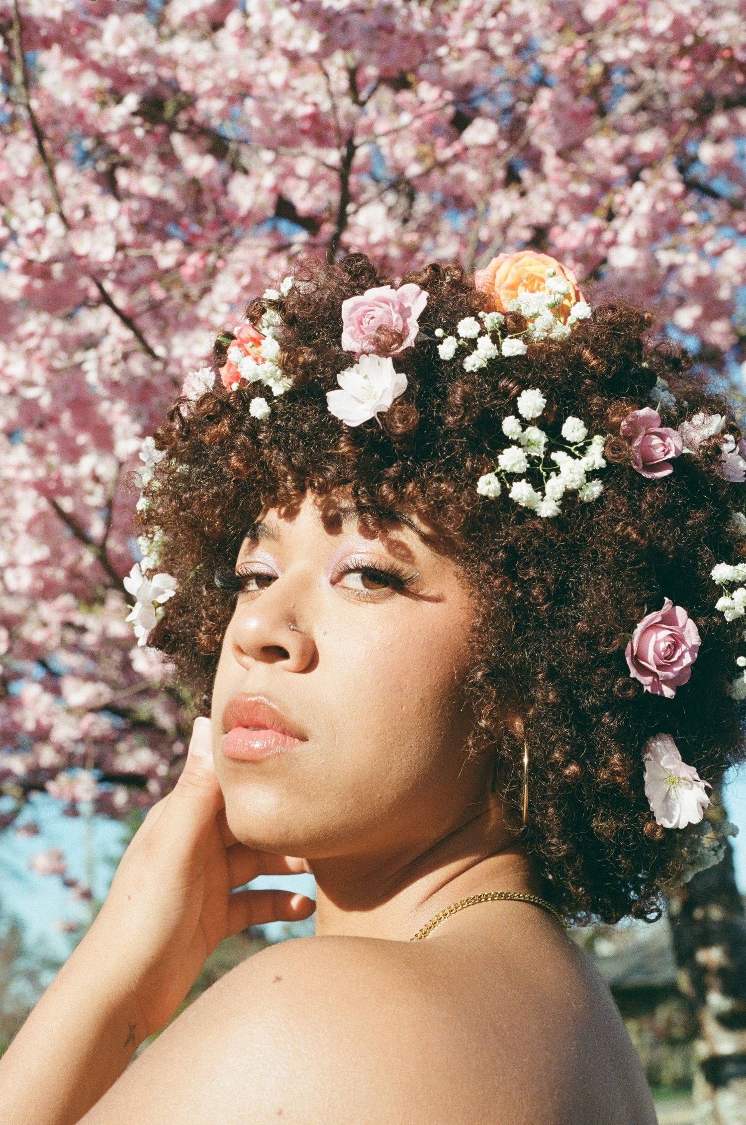 Portrait of a woman with flowers in her curly hair against blooming cherry blossoms.