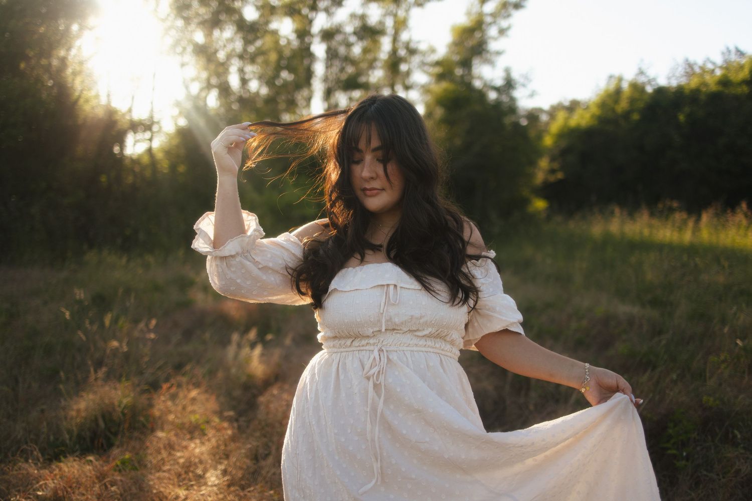 A person in a flowing white dress dances gracefully in a sunlit meadow at golden hour.