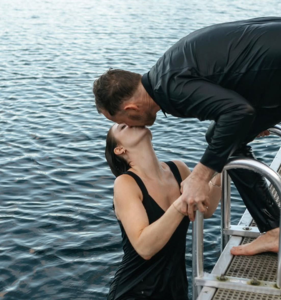 Romantic kiss between couple on boat deck over water.