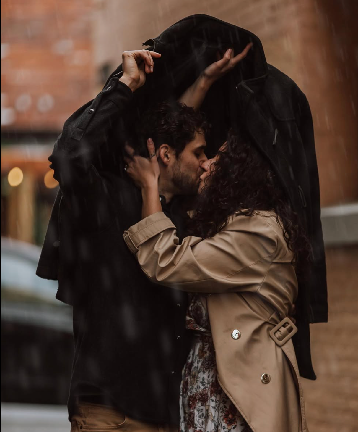 A romantic couple embracing in the rain with one person wearing a beige trench coat.