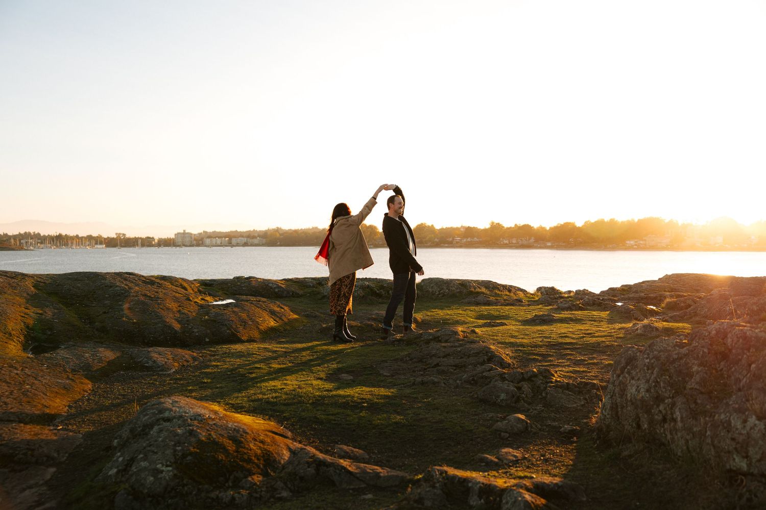 People walk along a scenic coastal trail during golden hour as the sun sets over the ocean.