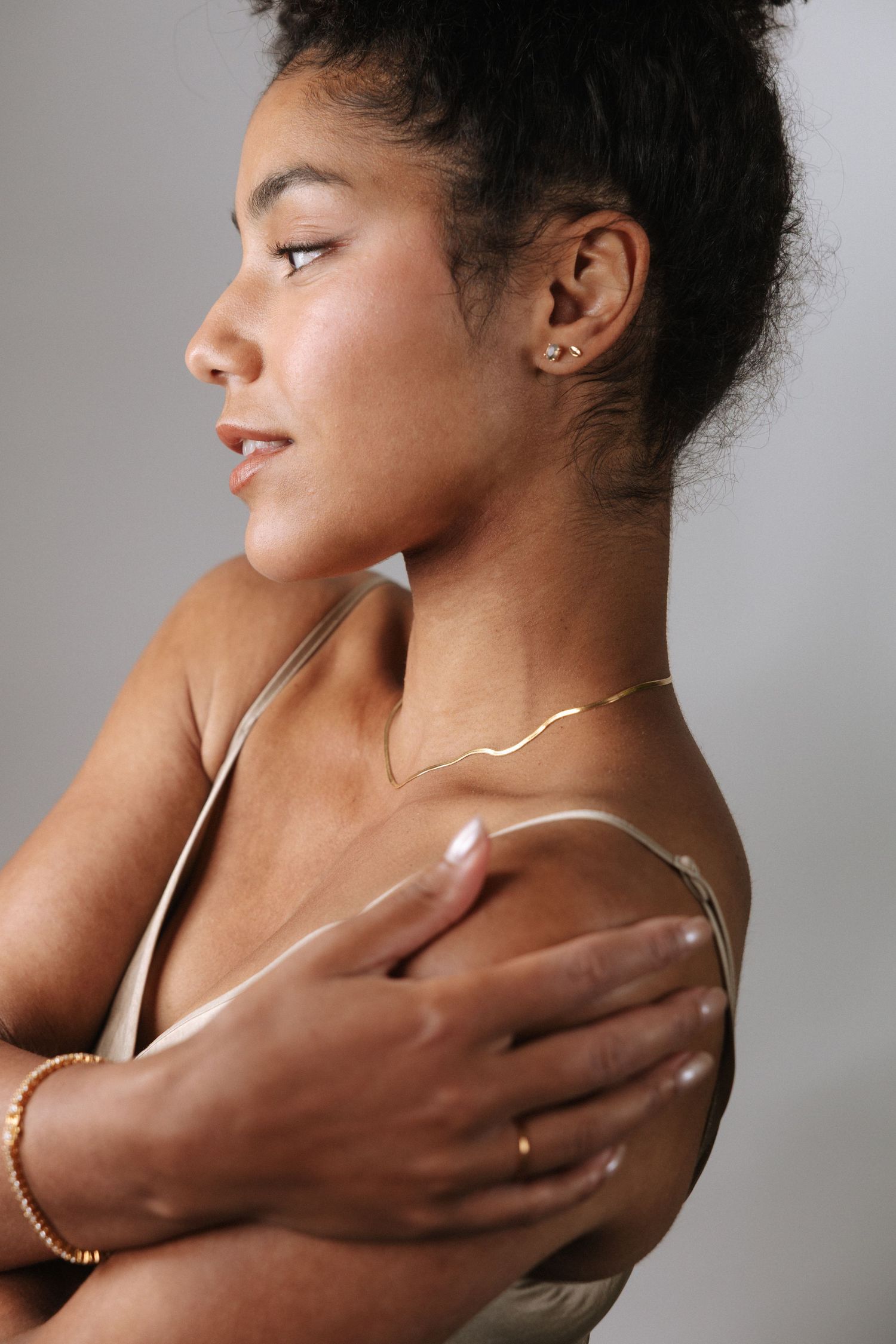 A series of profile shots showing a person's neck and shoulders adorned with delicate gold jewelry against a gray background.