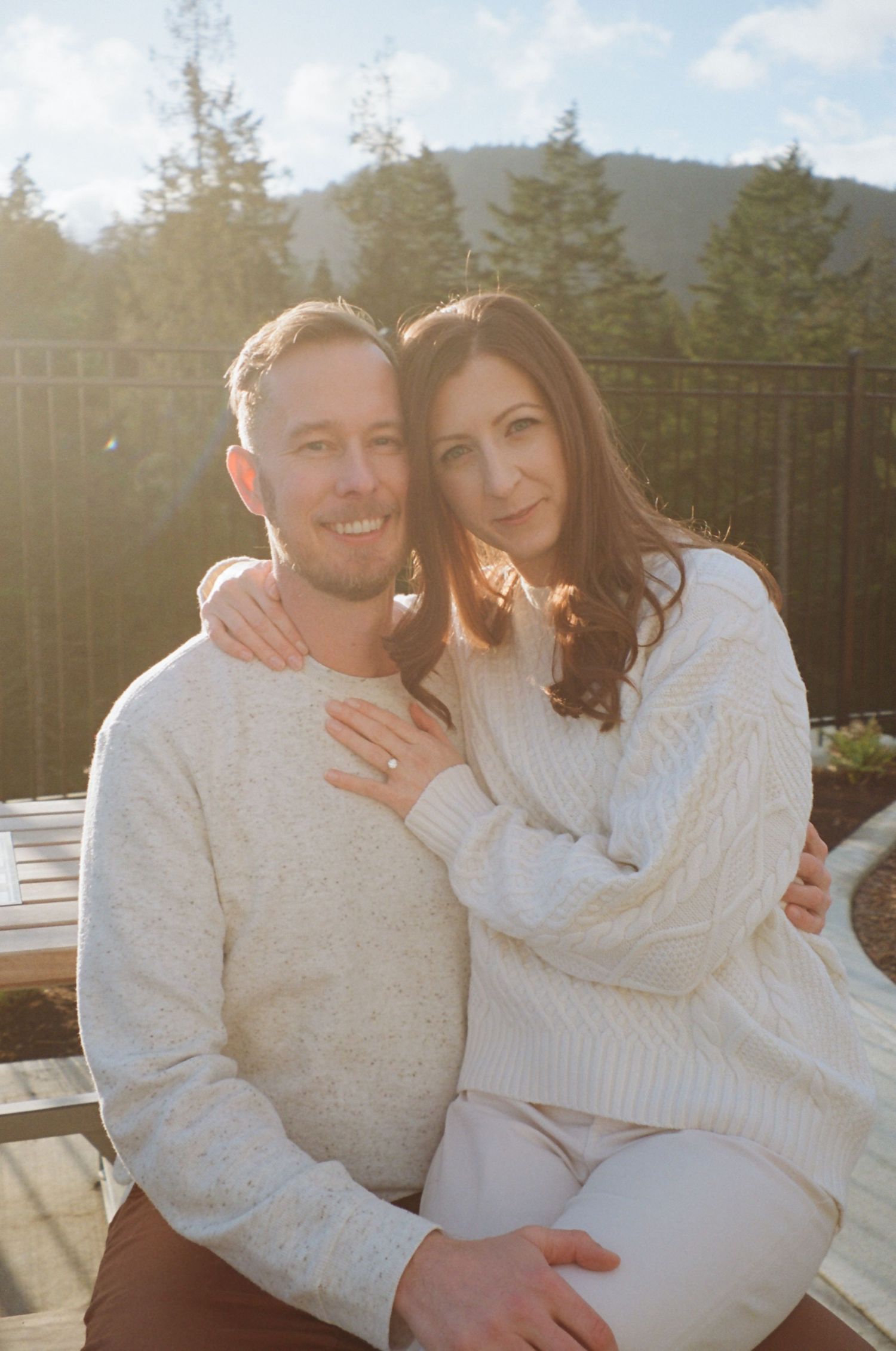 A couple in white sweaters share an intimate moment on a deck with mountain views.