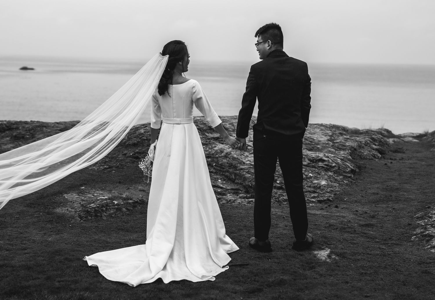 Dramatic black and white wedding photo of couple on coastal cliffs.