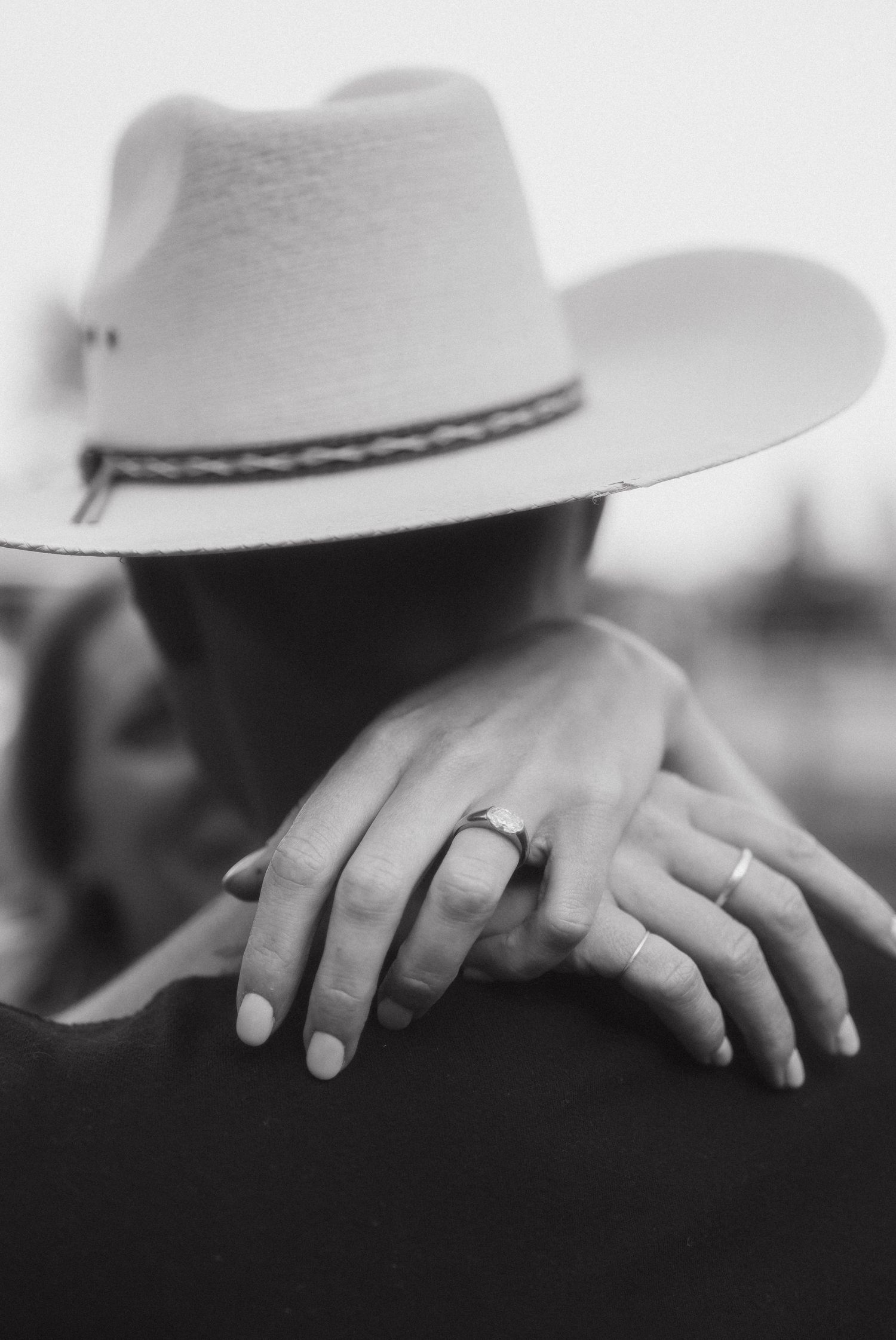 A black and white close-up photograph of hands resting on a surface with a white cowboy hat visible in the background.