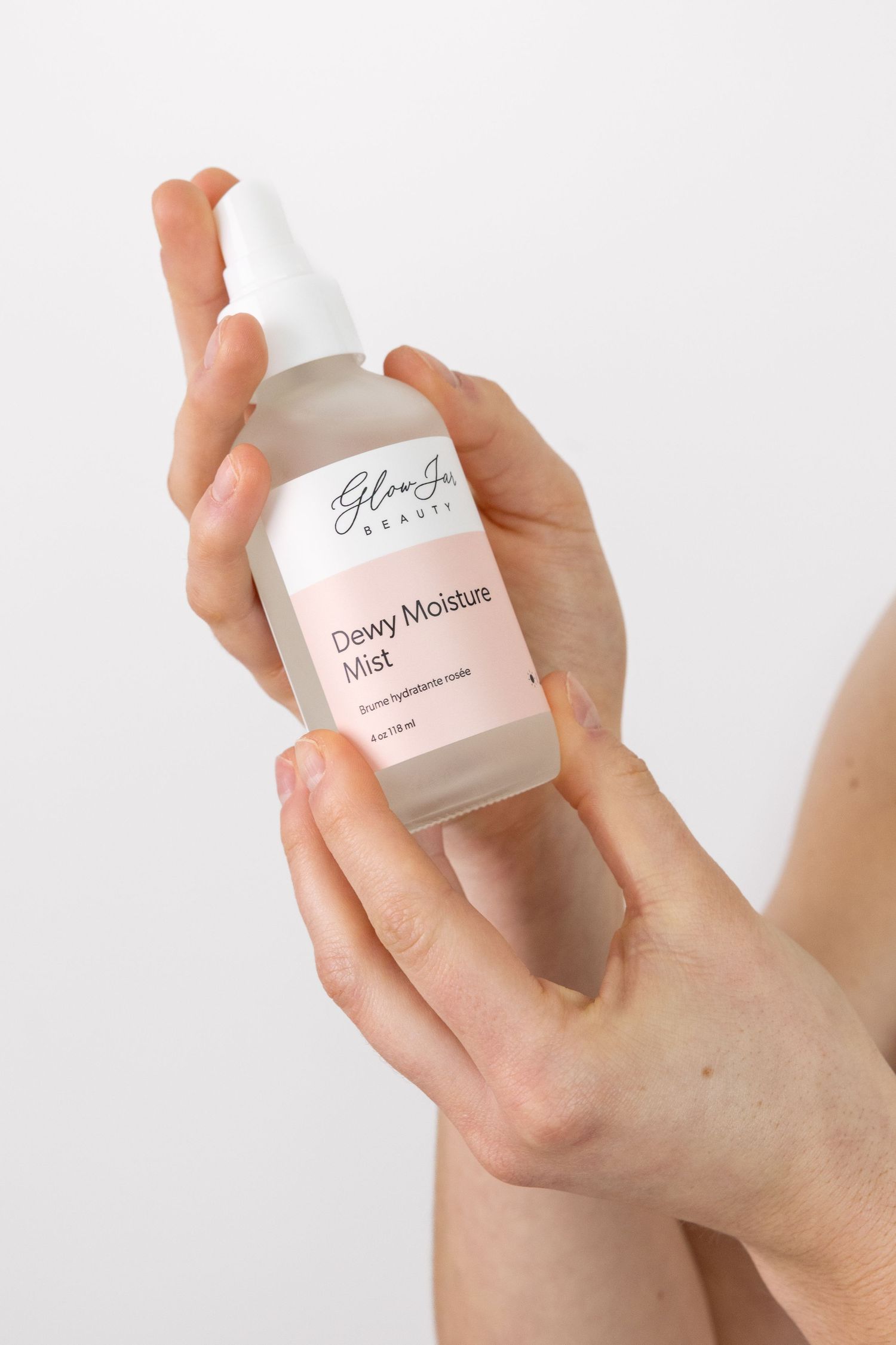 Hands holding a Glow Jo Beauty Dewy Moisture Mist spray bottle on a white background.