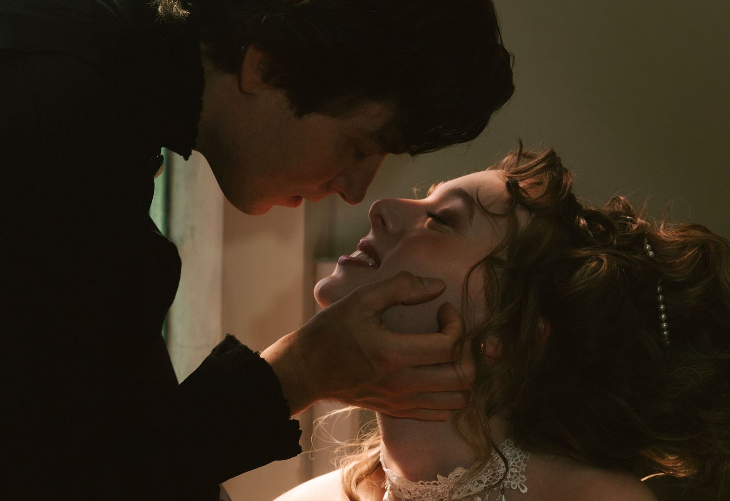 A man in a black suit leans in close to a woman with curly hair in a romantic, dramatic scene.