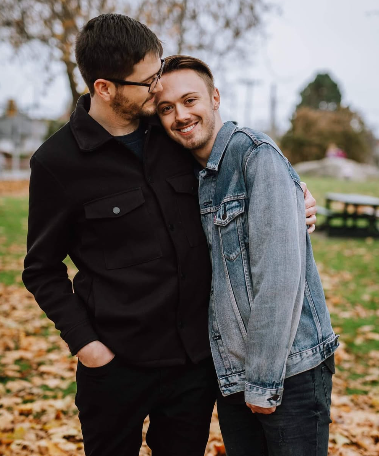 A couple sharing an affectionate moment among fallen autumn leaves.