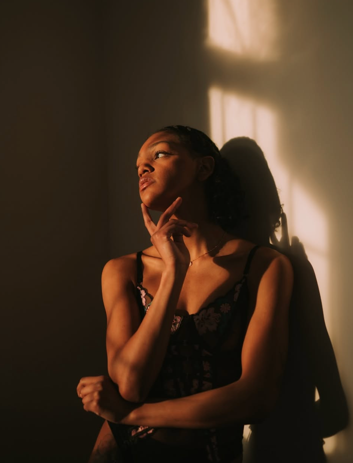 Dramatic portrait in golden sunlight against white wall creating shadow play.
