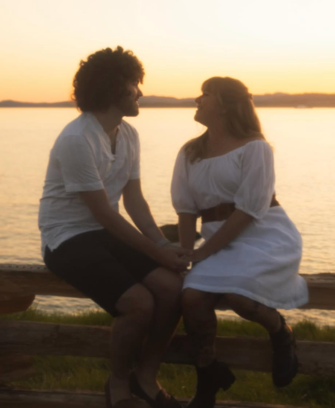 Couple in white clothing sharing intimate moment at sunset by waterfront.