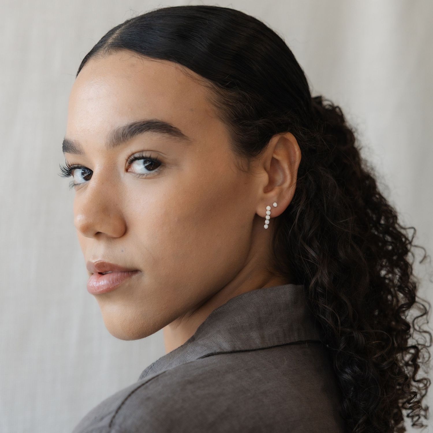 Side profile portrait of someone with curly dark hair and hoop earrings against a light background in multiple poses.