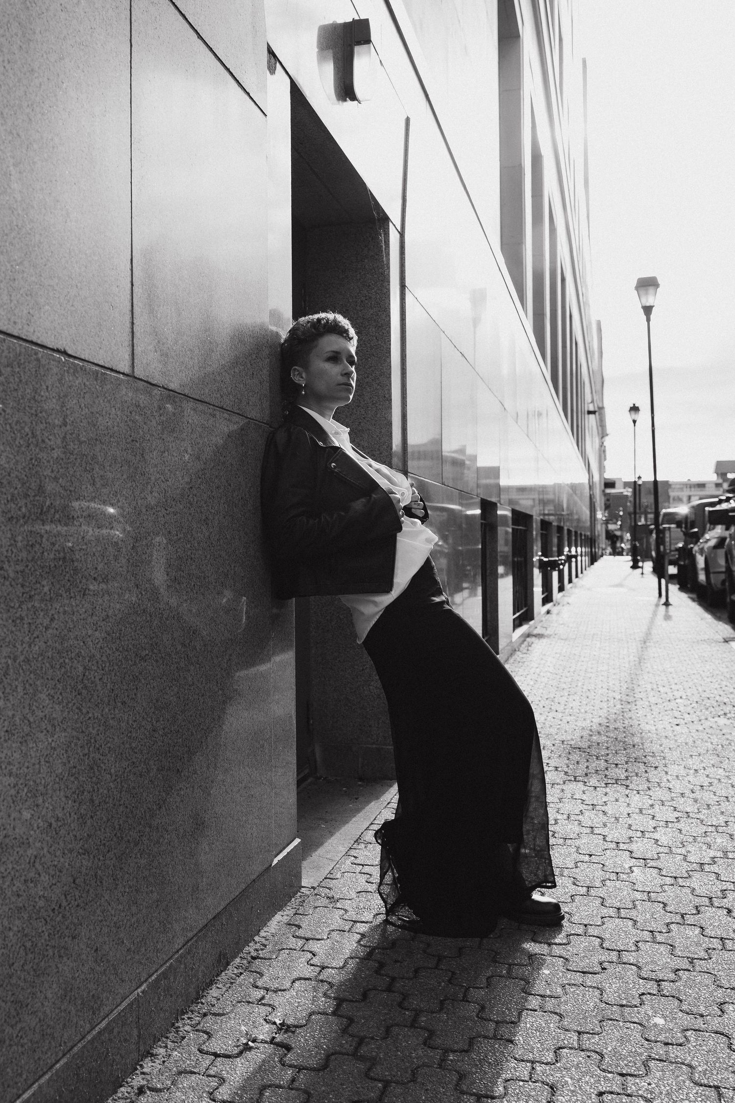 A black and white photo sequence shows a figure sitting against a wall on a paved sidewalk in an urban setting.