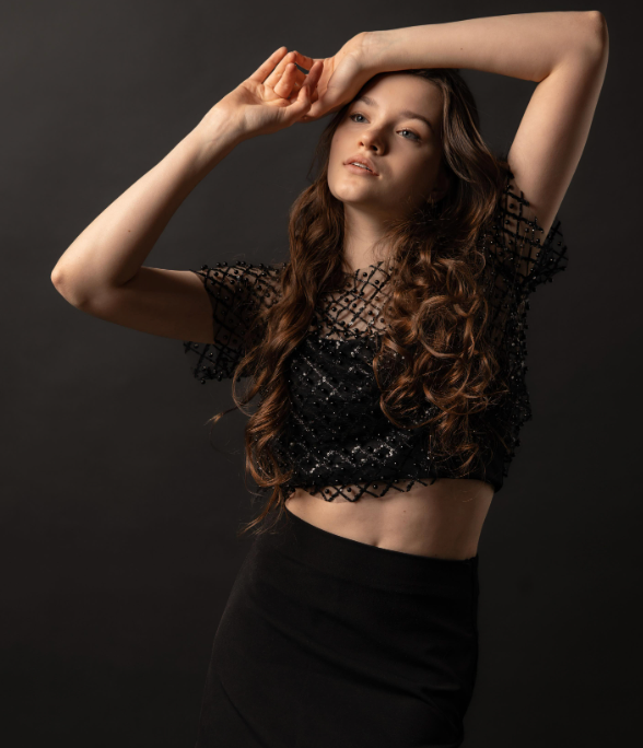 Woman in black lace crop top poses dramatically against dark background.