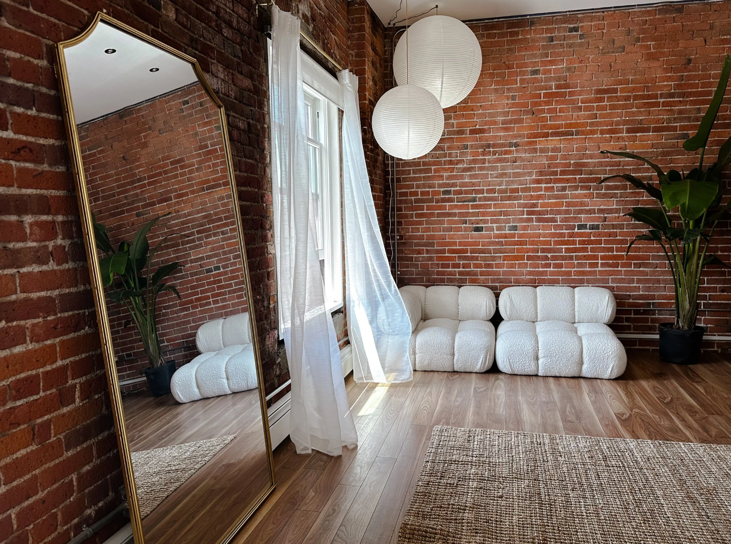 Good Juju Studio Modern yoga studio interior with exposed brick walls, white curtains, and round pendant lights.