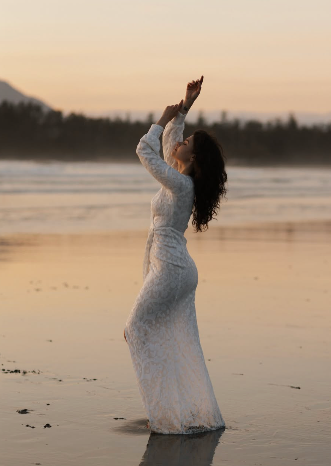 Silhouette of woman in white dress posing gracefully on beach at sunset.