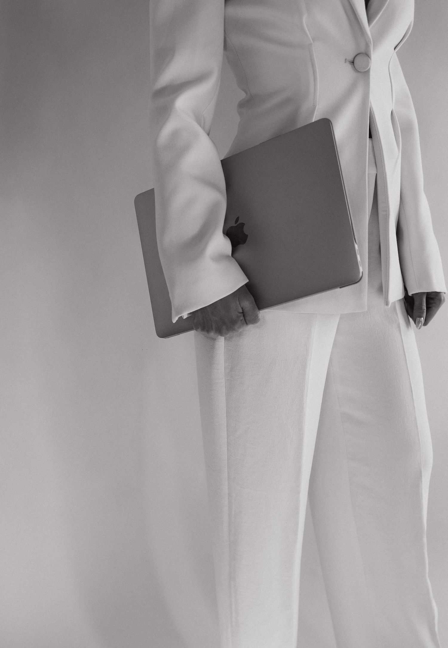 Professional figure in crisp white suit holds a sleek laptop against minimalist background.