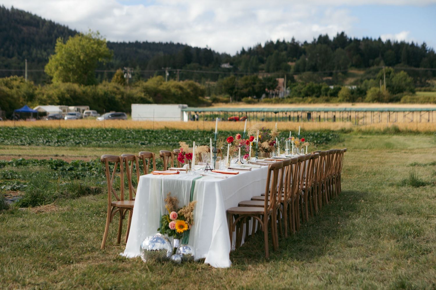 Elegant outdoor dining table with white linens and wooden chairs set against a scenic mountain landscape backdrop.