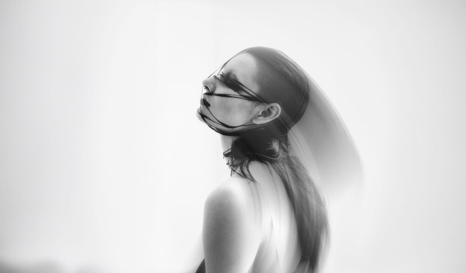 Black and white photo of a woman wearing a face mask, with a blurred motion effect creating a ghostly double exposure.