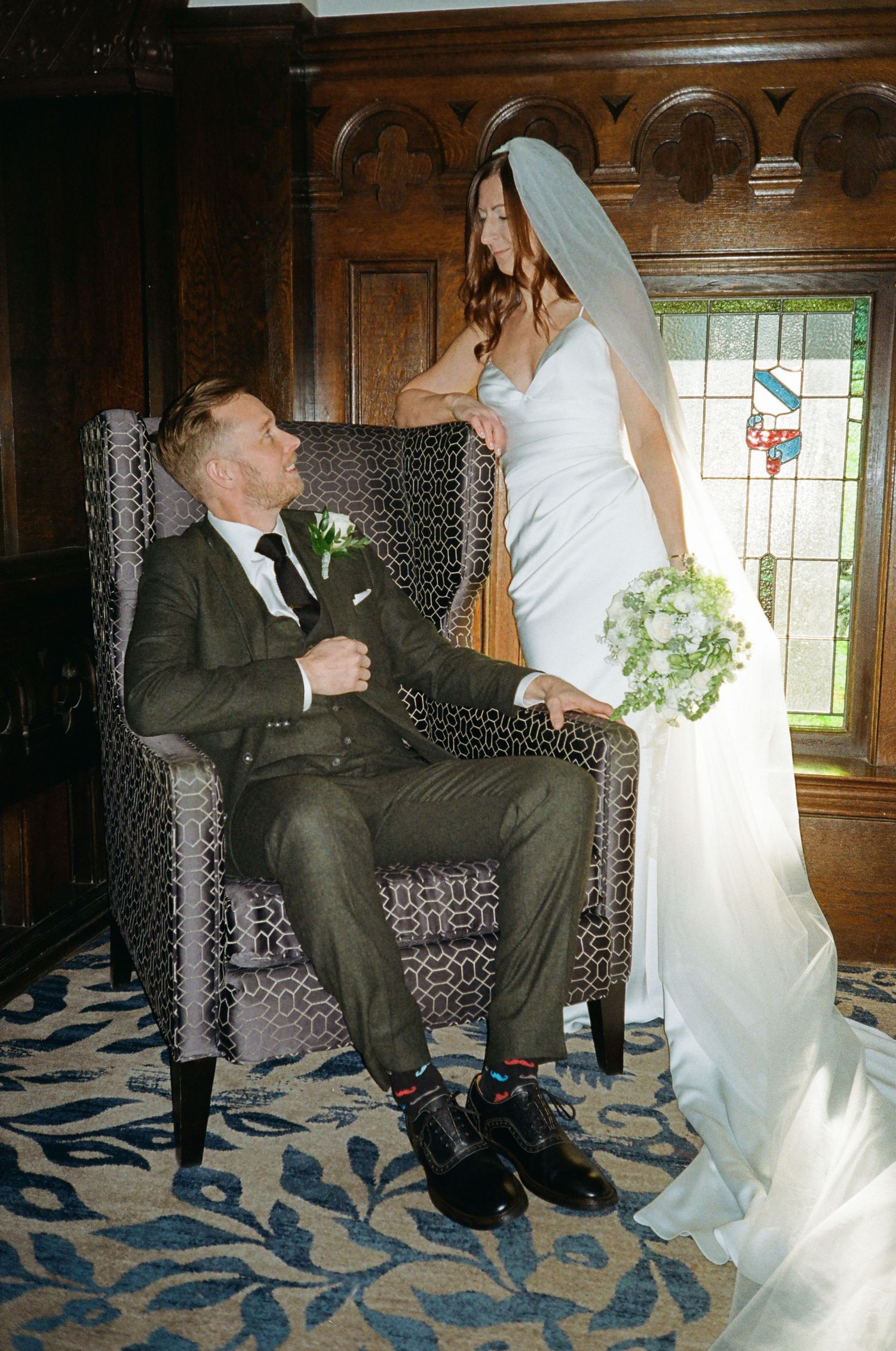 A romantic wedding moment captured between a bride and groom in an elegant room with stained glass windows.