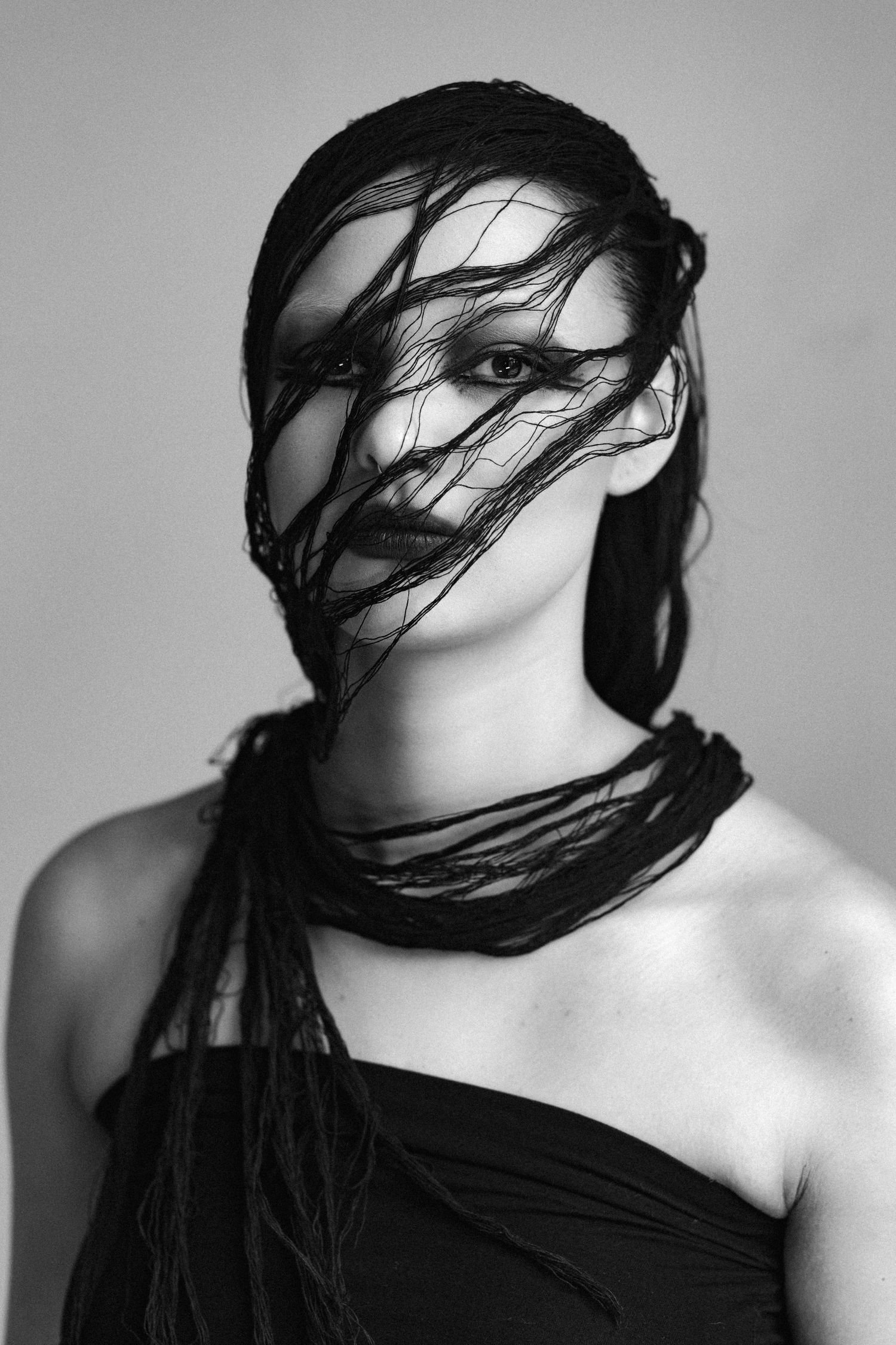 Black and white portrait of a woman with dark fabric wrapped dramatically around her face and neck.