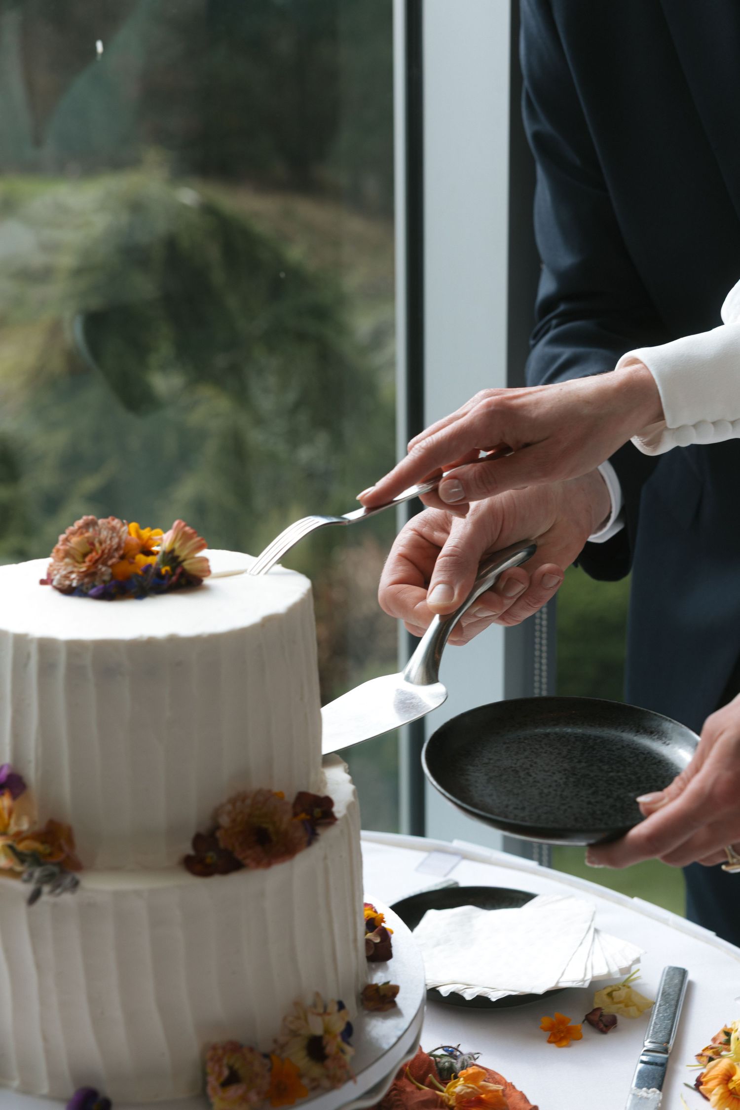A series of hands cutting into a white wedding cake decorated with orange and yellow flowers.