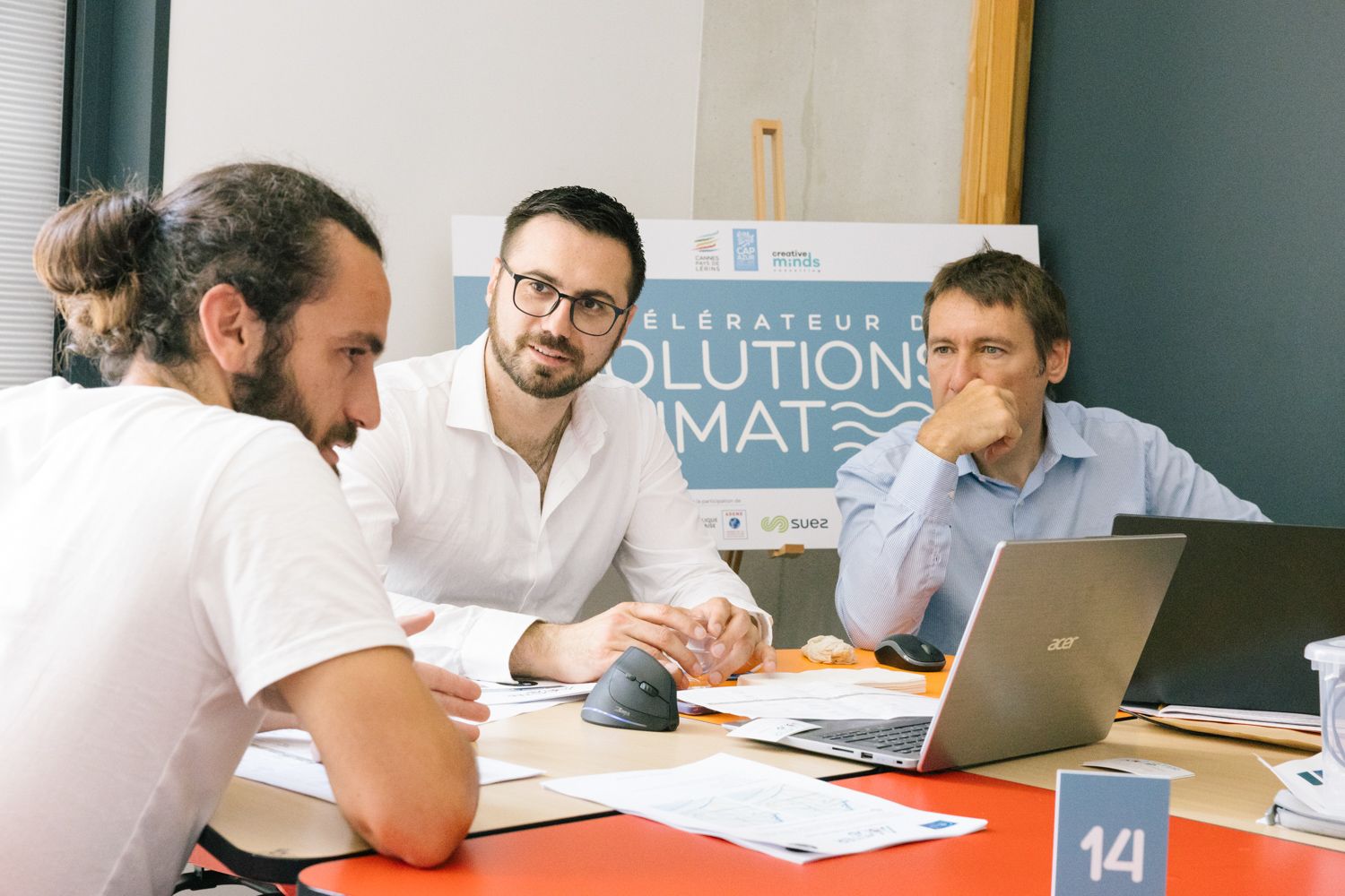 Three professionals collaborate on a project during a business meeting at a desk with laptops.