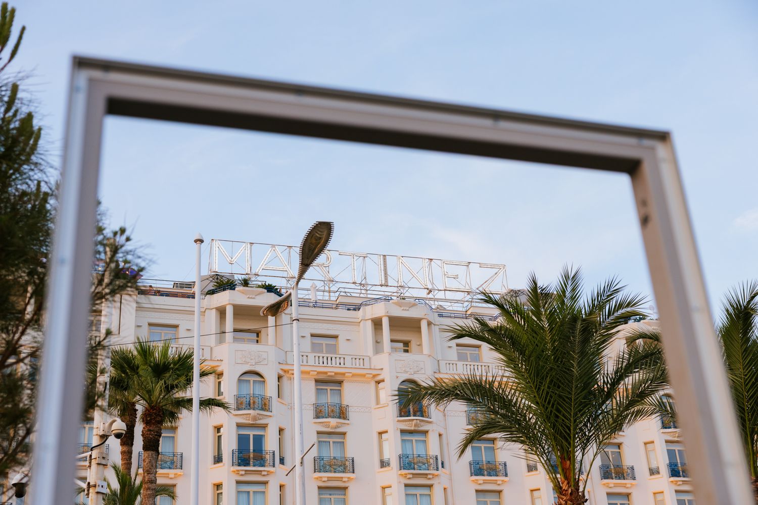 White Mediterranean-style resort buildings with balconies and palm trees against a bright blue sky.