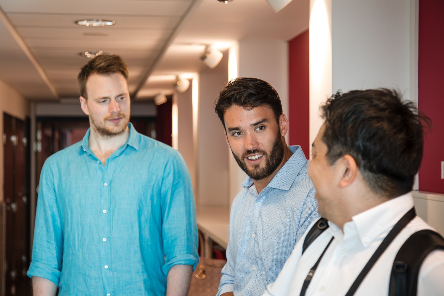 Three professionals having a discussion in an office hallway.