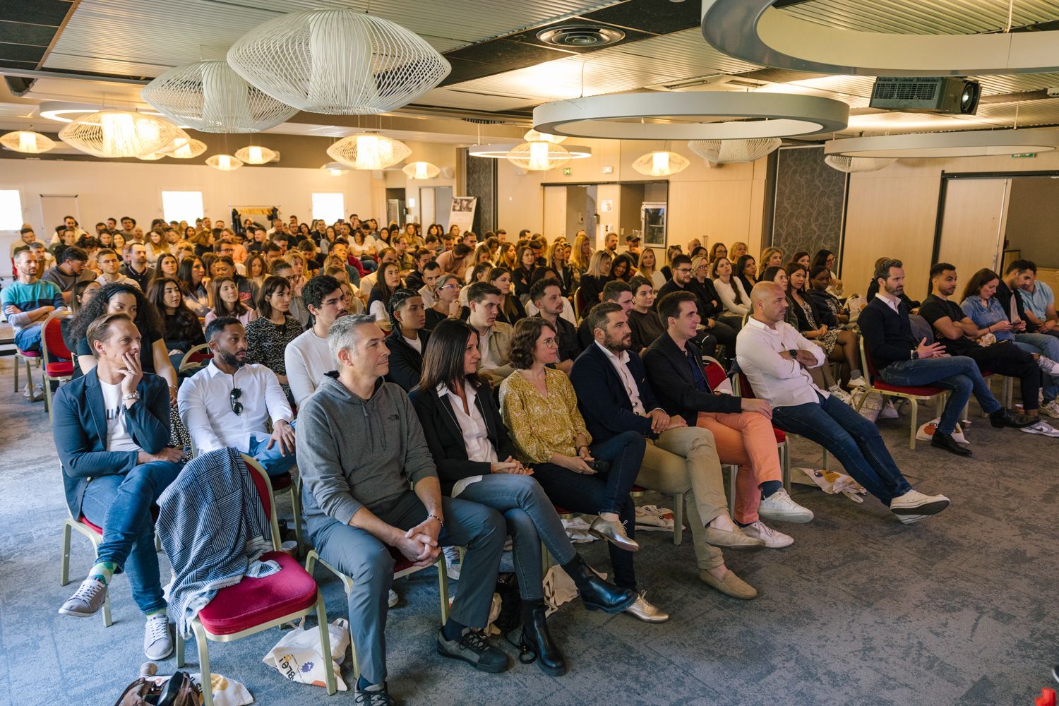 Packed conference room filled with attendees watching a presentation in a modern office space.
