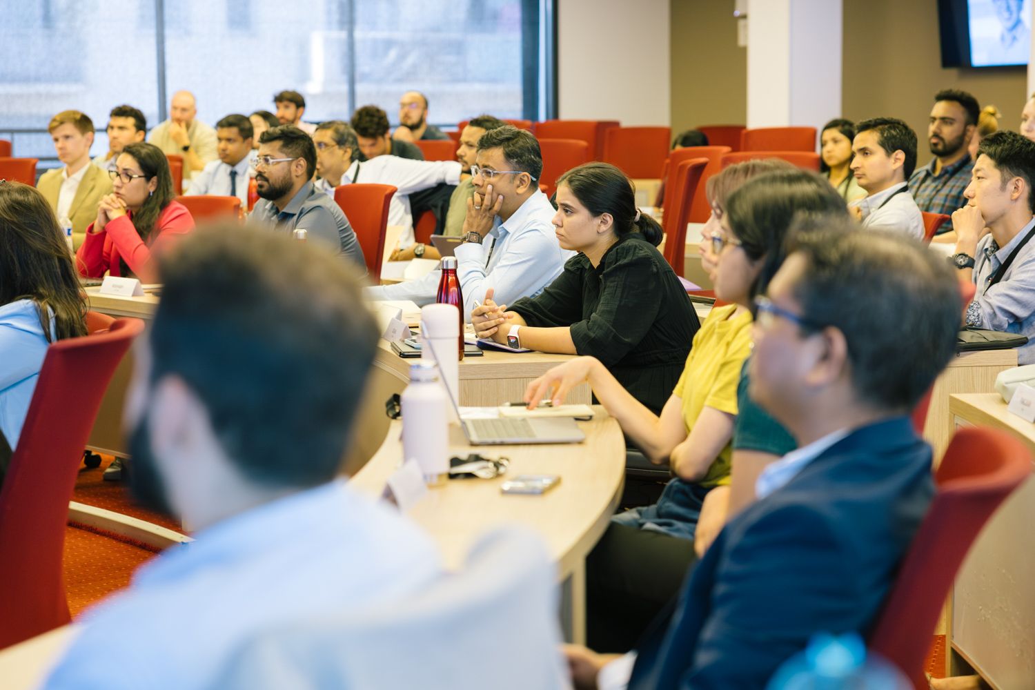 Diverse group of students attending lecture in classroom with red chairs.