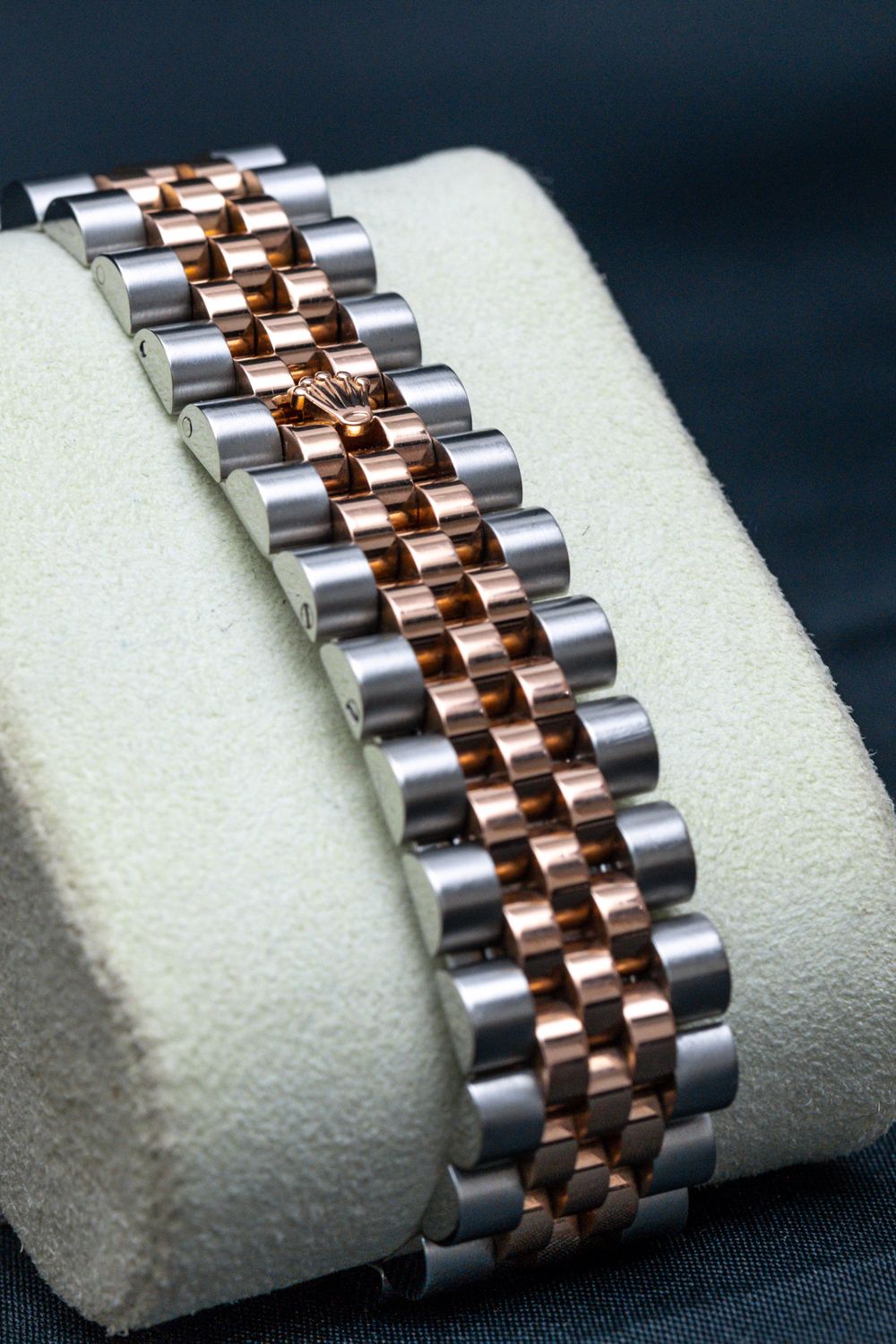 Close-up of a luxury watch bracelet with two-tone stainless steel and rose gold links on a cream display cushion.