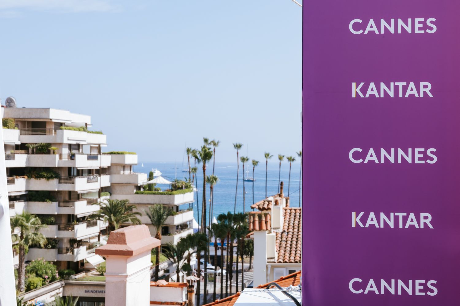 Purple Kantar branded banners displayed at a beachfront location in Cannes with palm trees and buildings visible.