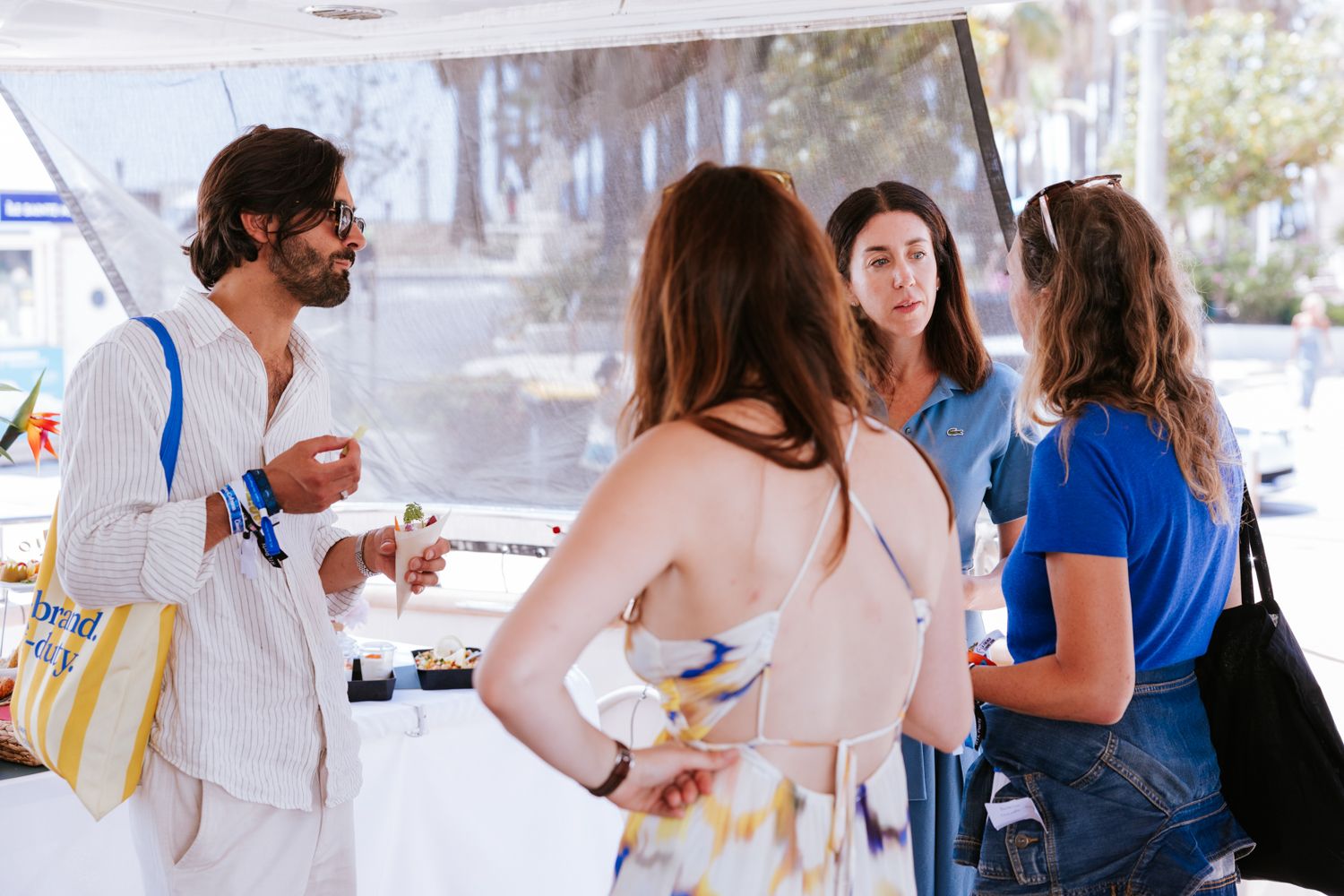 Guests mingle and socialize at an outdoor event with white tables and chairs under a covered patio area.