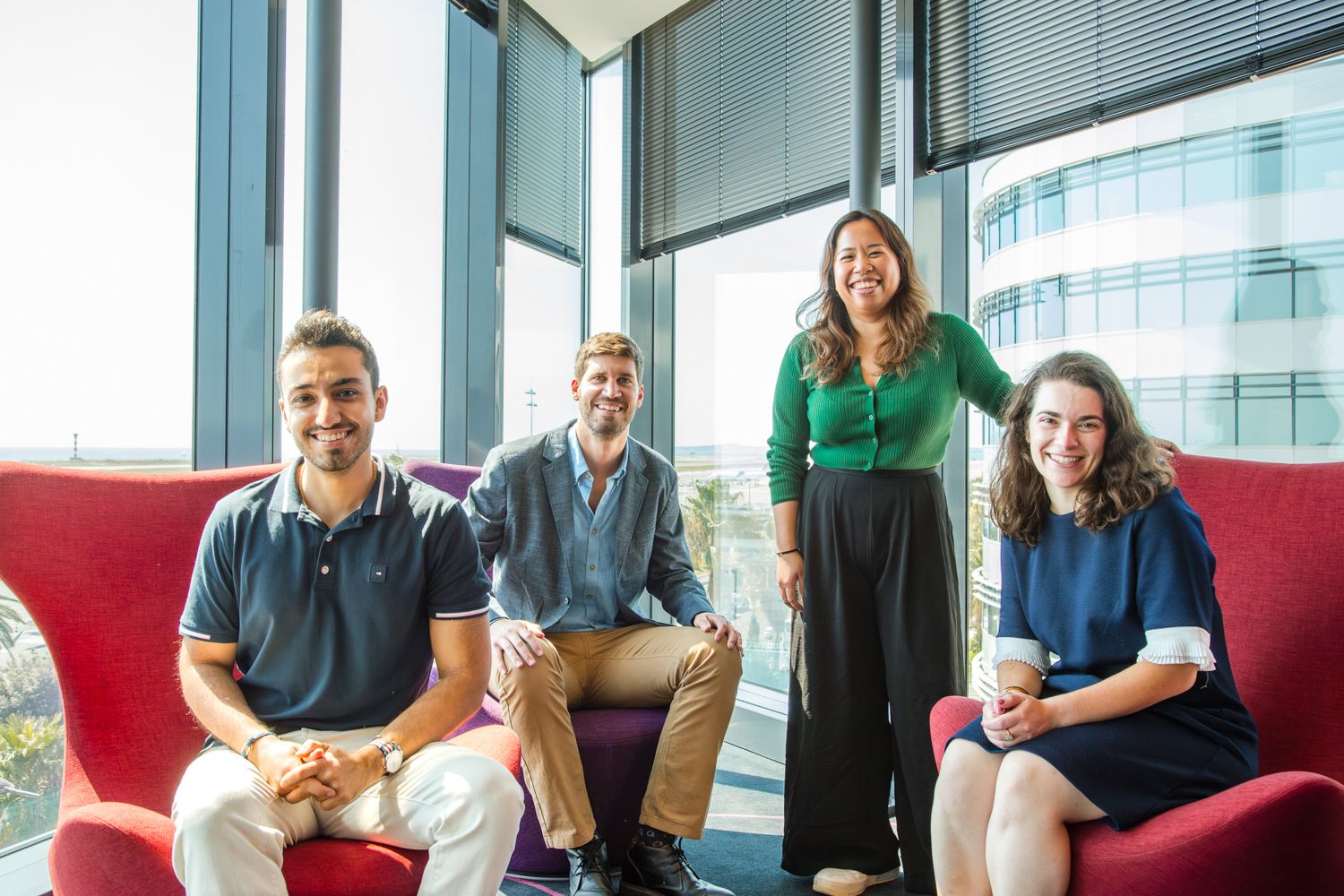 Team members relaxing on red couches in a bright corner office space.