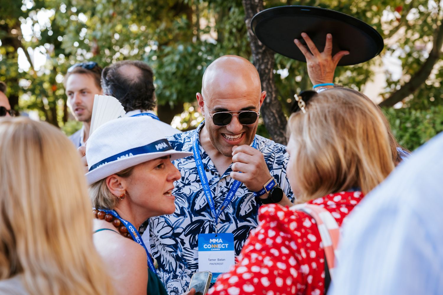 A group of people in casual summer attire gather outdoors in a social setting during daytime.