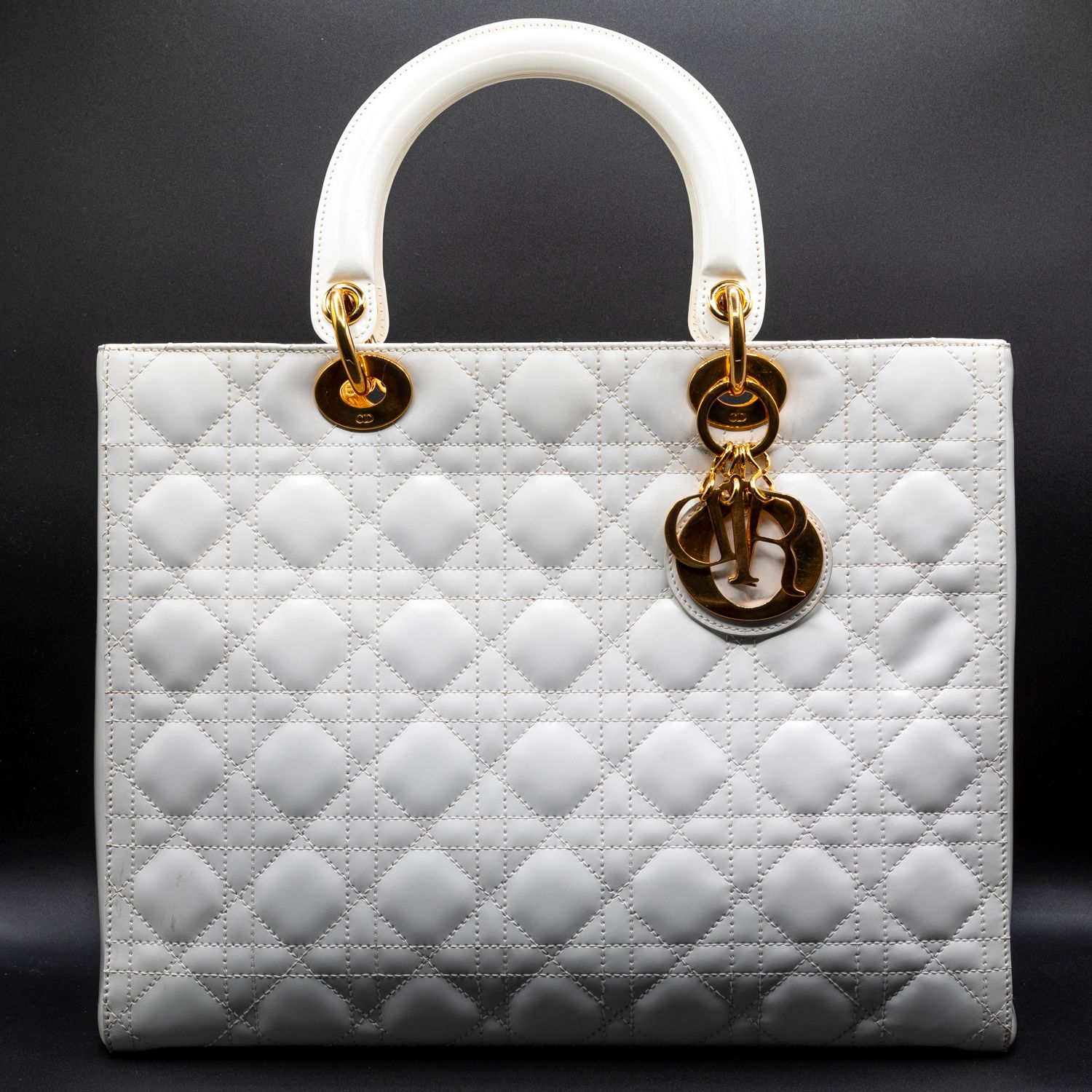 White quilted Lady Dior handbag with gold hardware against dark background.