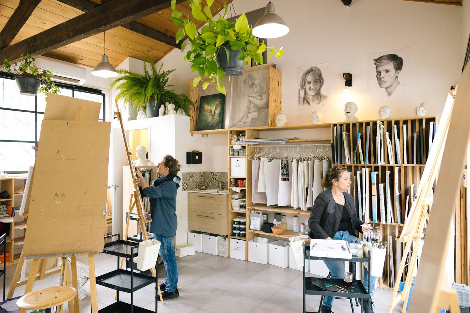 Interior view of an art studio with easels, plants and artwork on walls.
