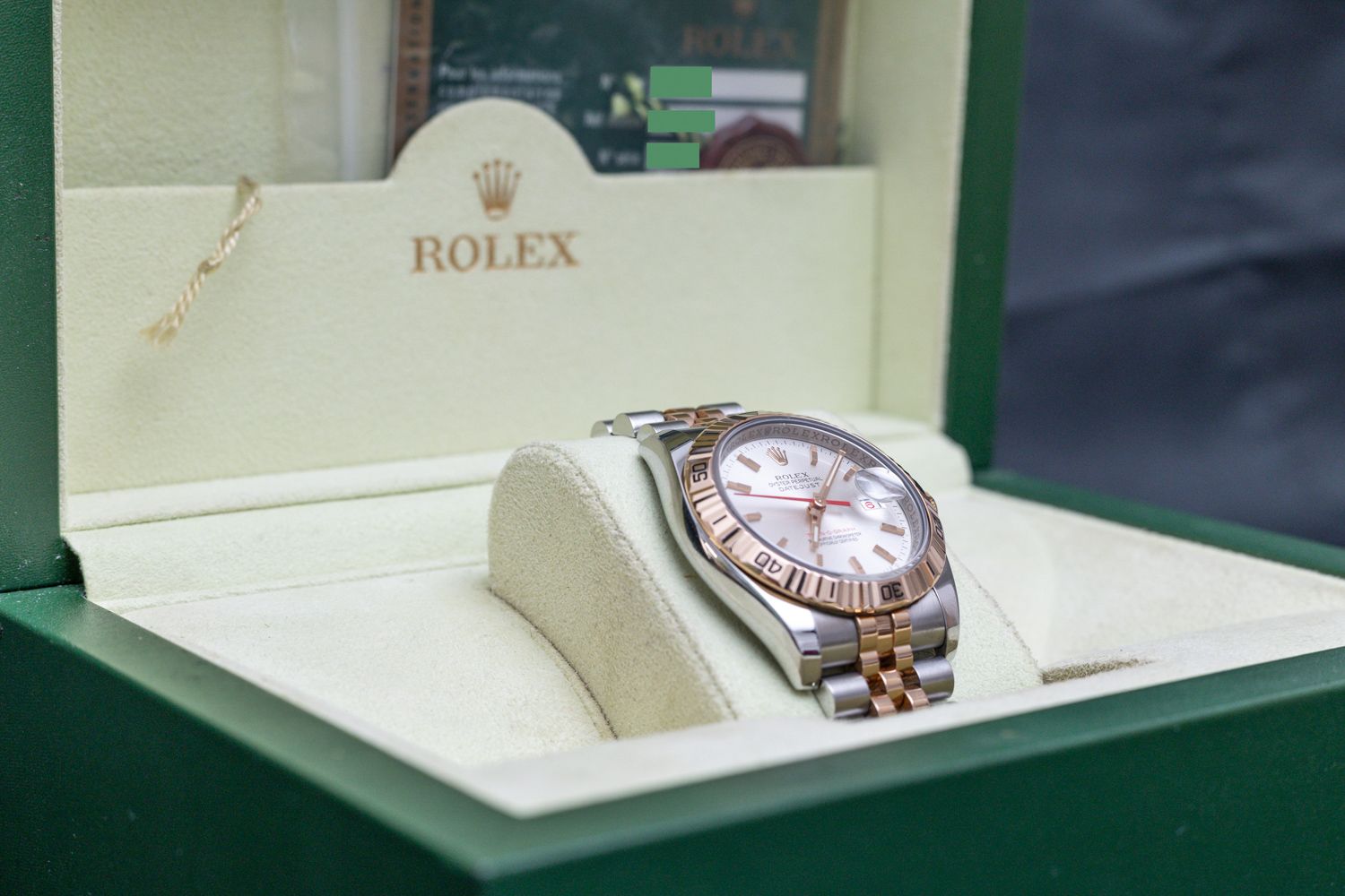 Rolex watch with two-tone bracelet displayed in a green branded box on cream cushion.