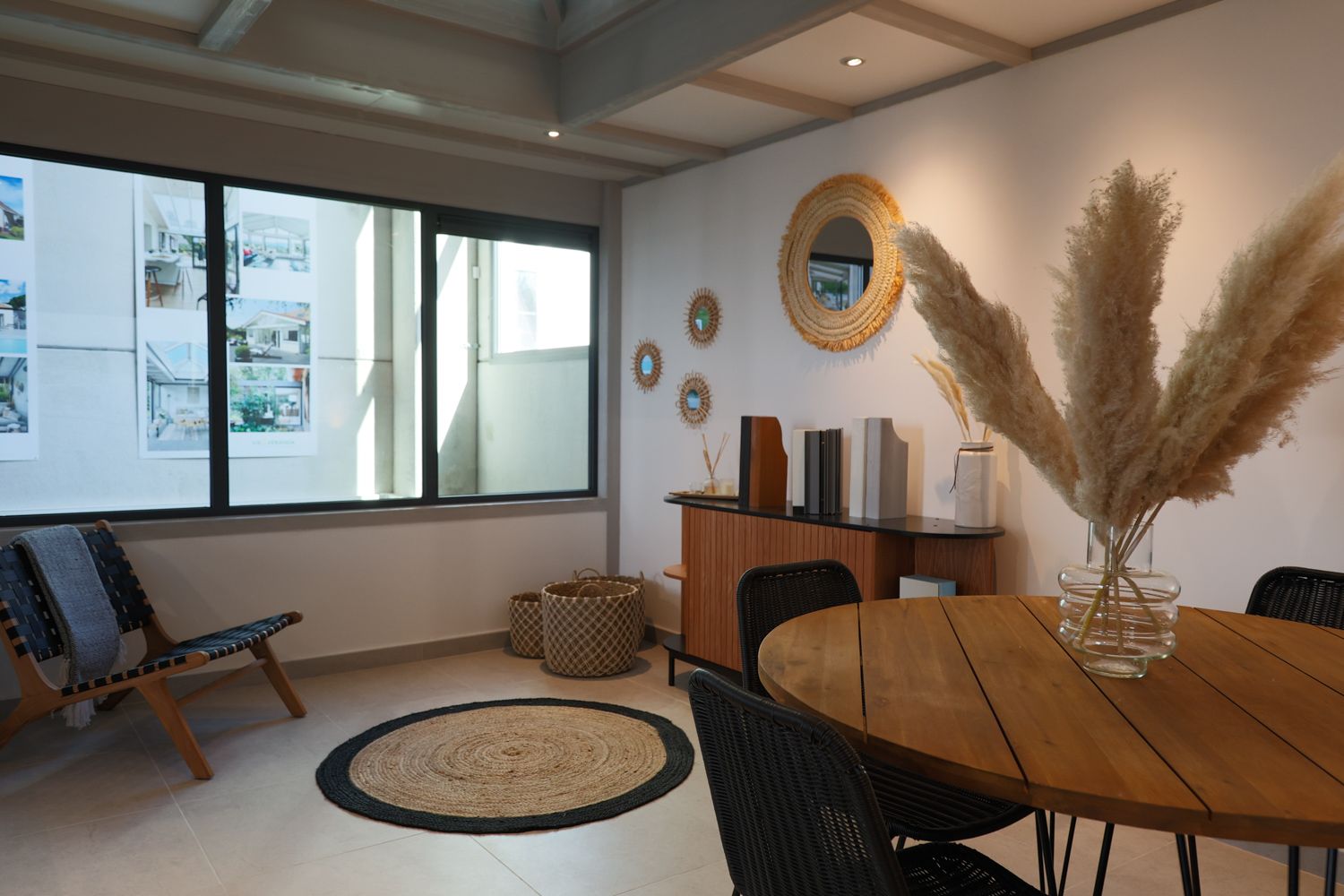 Modern interior space with round mirror, wooden dining table, and decorative pampas grass arrangement.