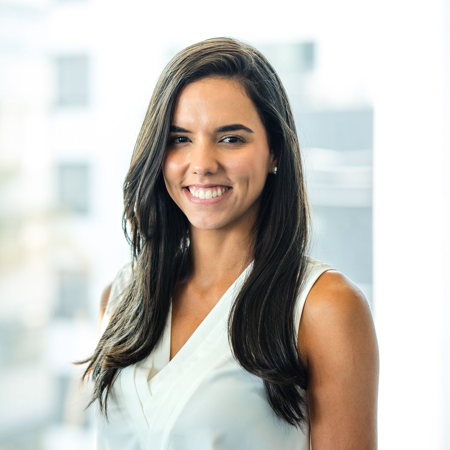 Professional headshot of a person in white sleeveless top against office setting.