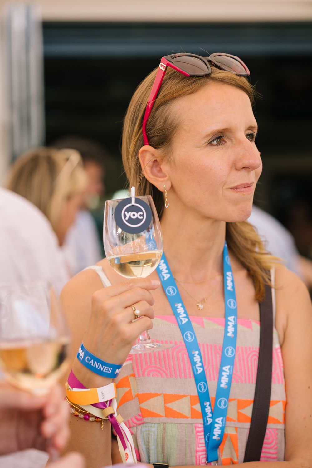 Attendee holding wine glass with YOC branding at sunny outdoor event.