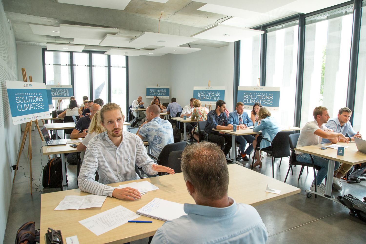 A bright modern office space with multiple people working at tables during a business event.
