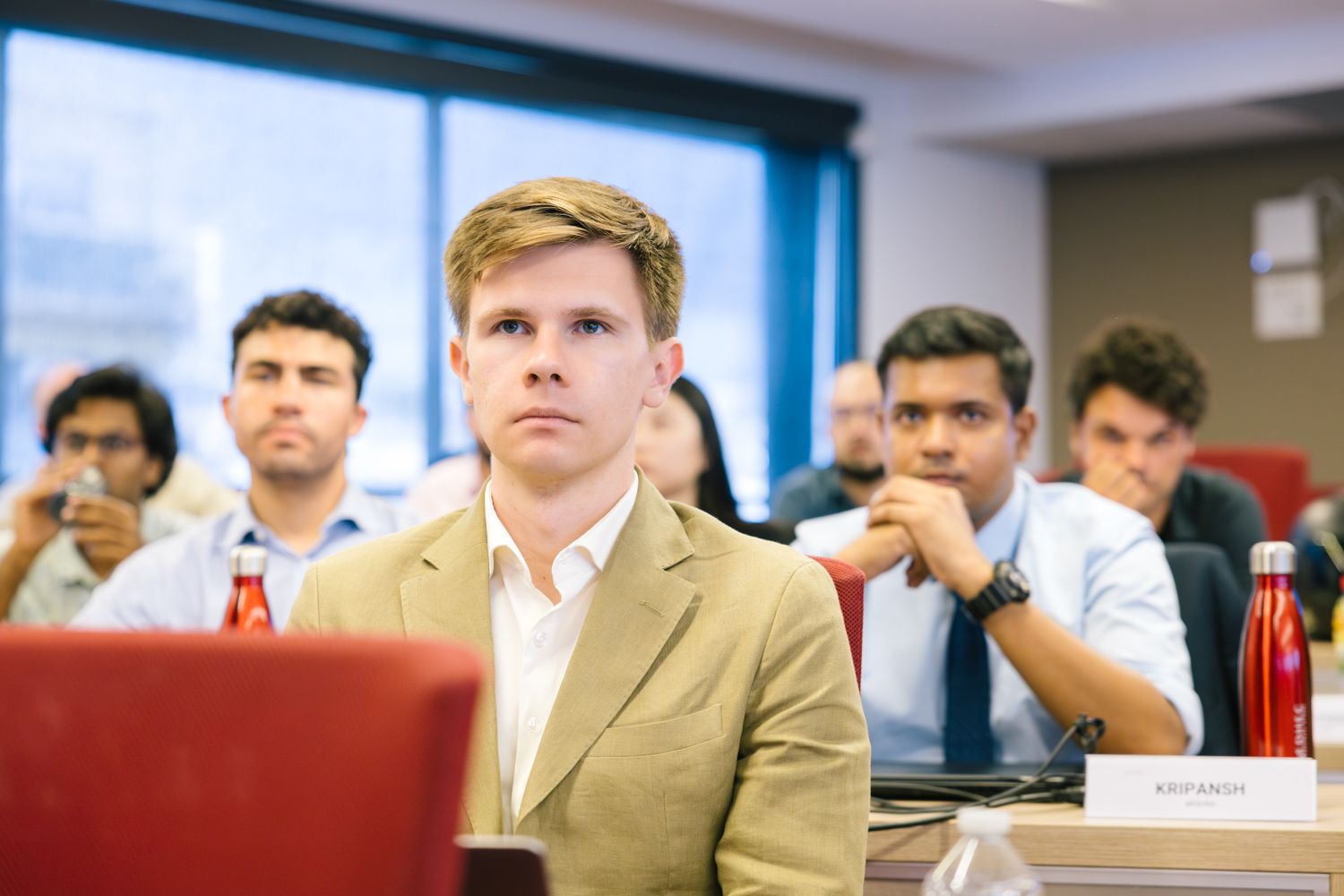 Students listening attentively in lecture hall with red seats.