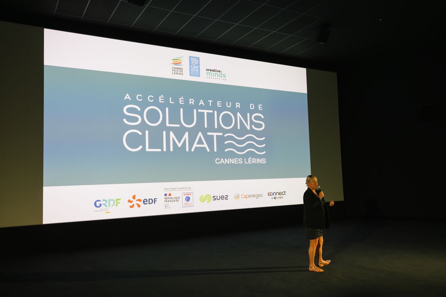 Presenter speaking at Solutions Climate conference in front of large projection screen.