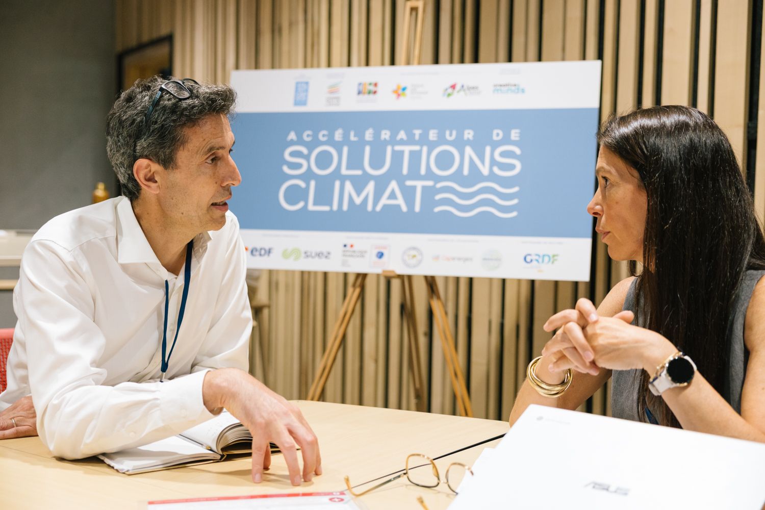 Two professionals engaged in discussion at a climate solutions conference with banner visible in background.