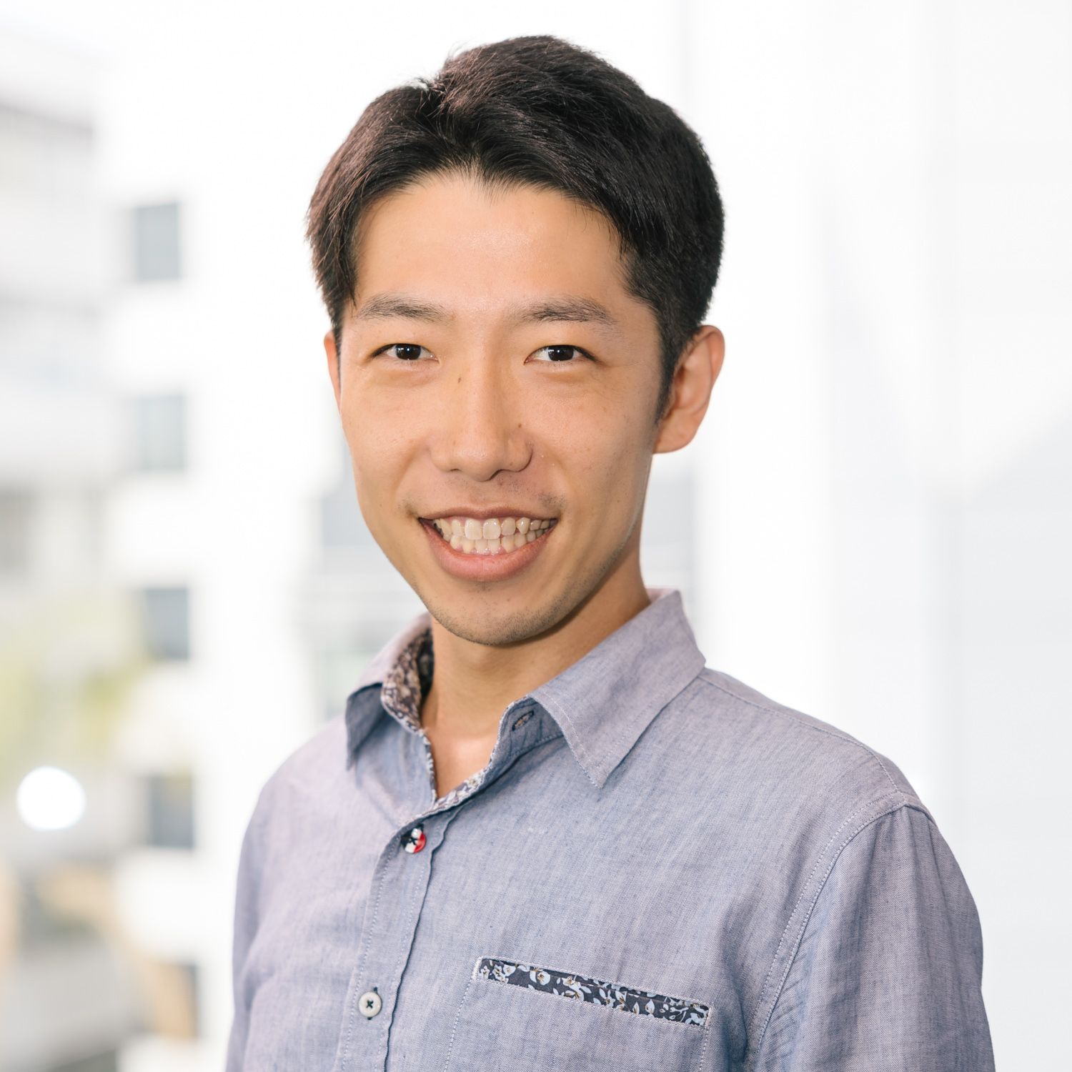 Business professional in grey shirt smiling in bright office environment.