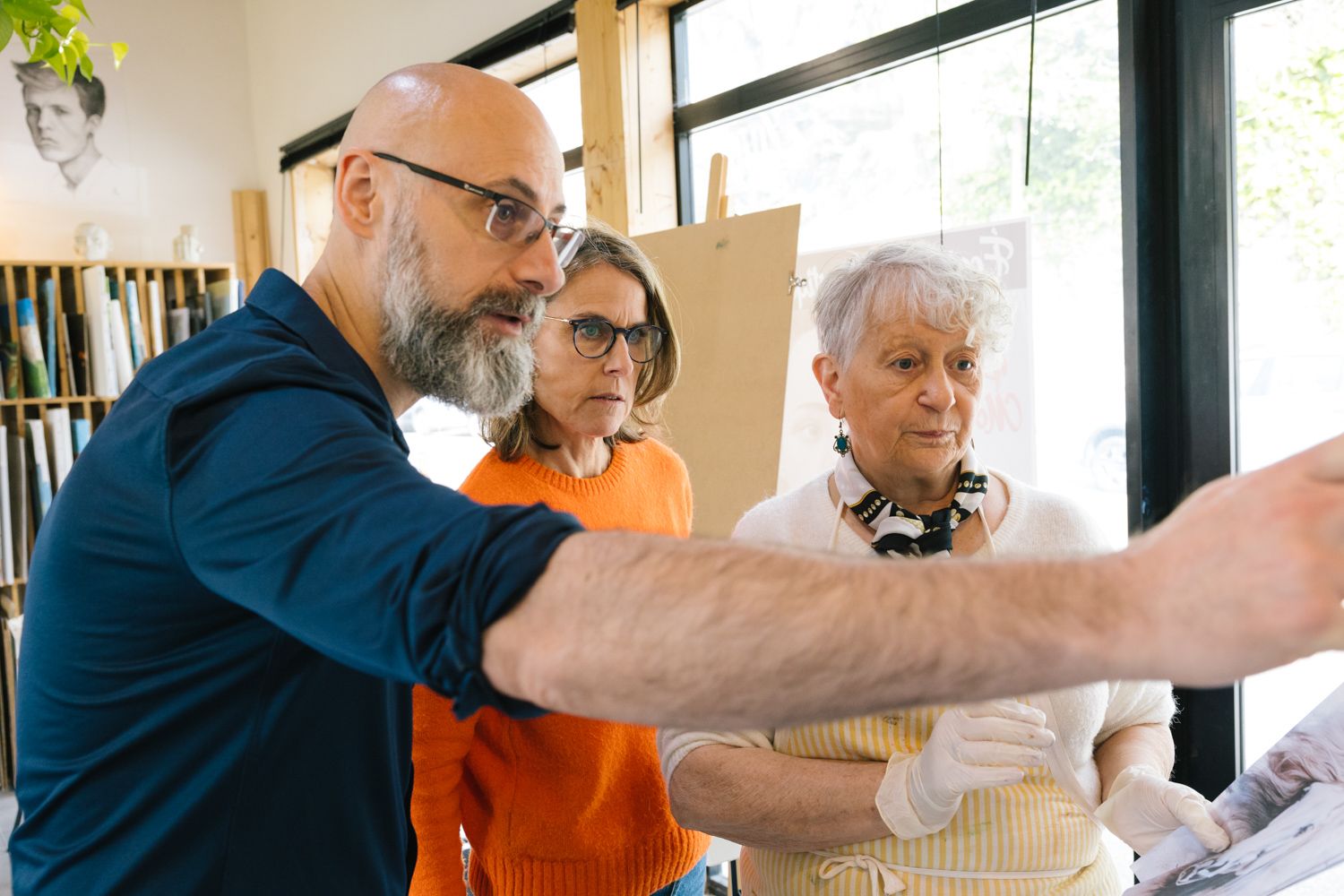 Art instruction session with three people examining artwork in a studio.