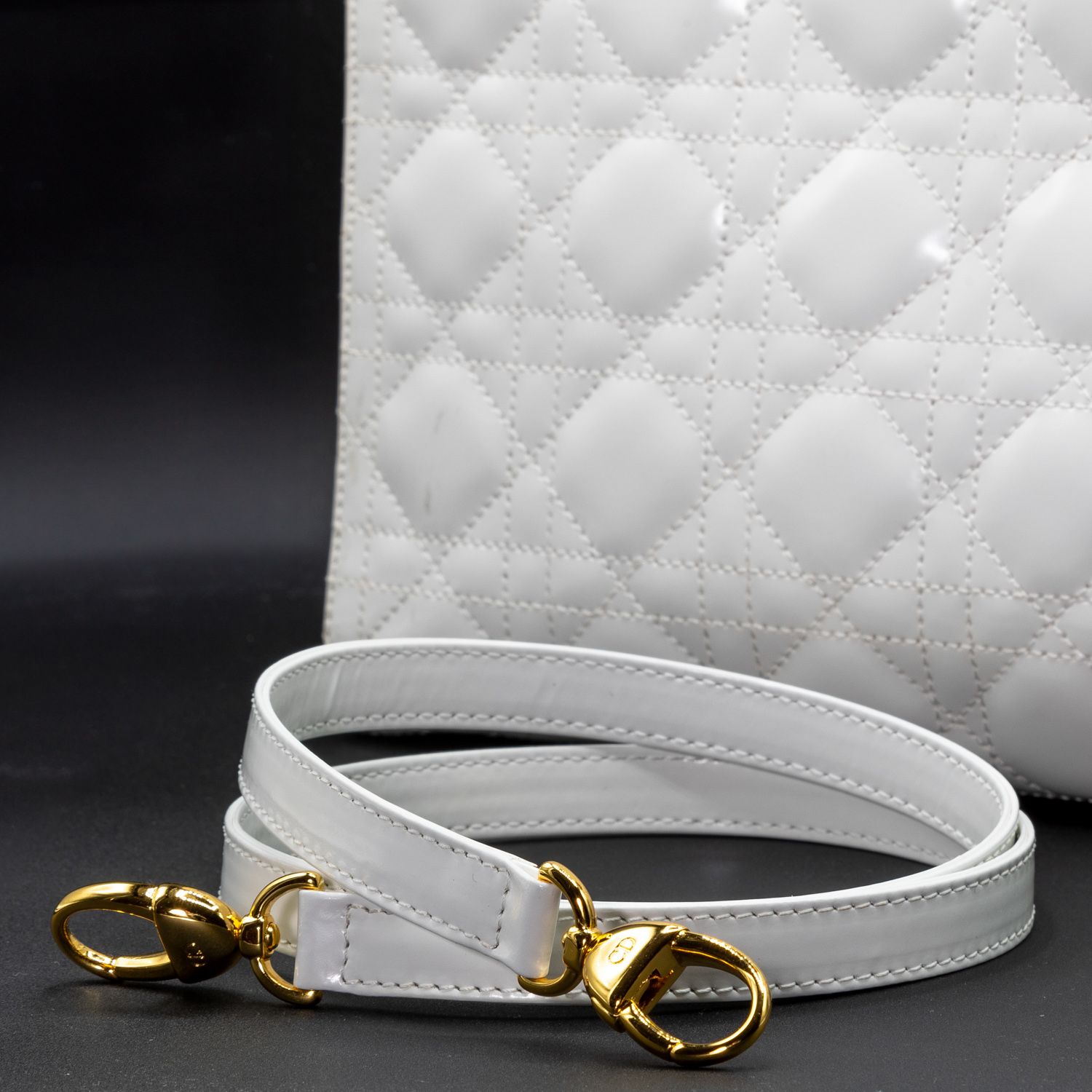 White leather shoulder strap with gold hardware attachments on black background.